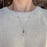 Necklace with star and teardrop pendant worn by a person in a light gray sweater.