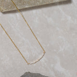 Delicate gold chain necklace with small freshwater pearls on a light stone surface
