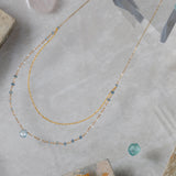 Gold necklace with blue aquamarine and moonstone beads on a textured surface