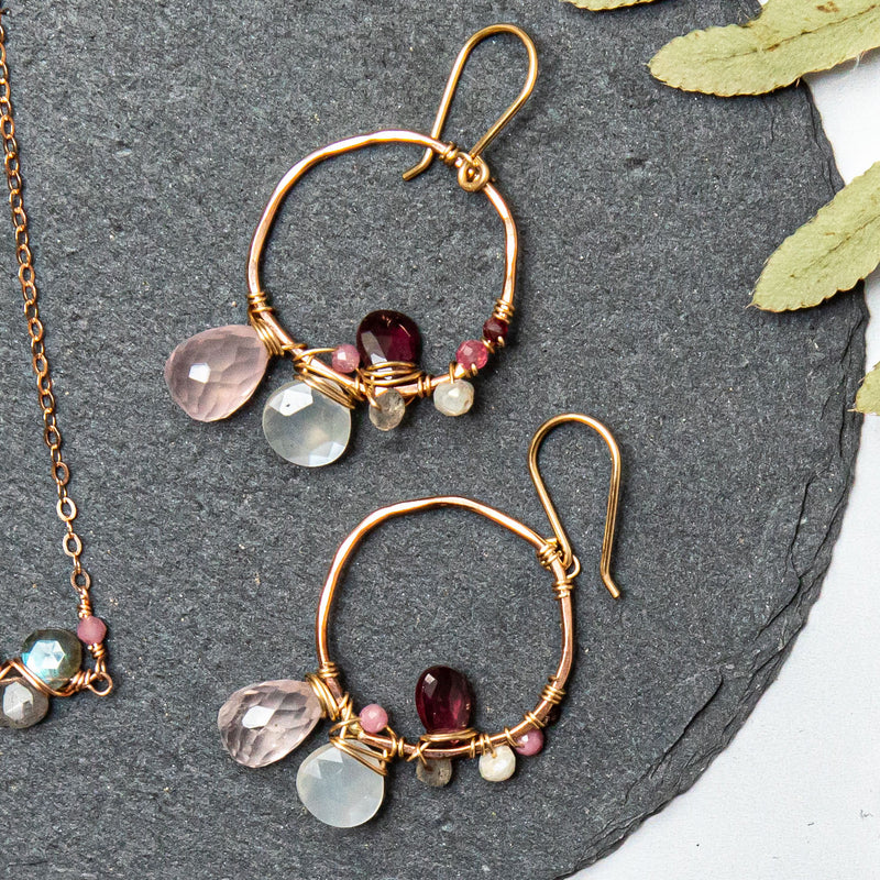 Gold and rose gold hoop earrings with asymmetrical gemstone wraps including rose quartz, moonstone, and rhodolite garnet
