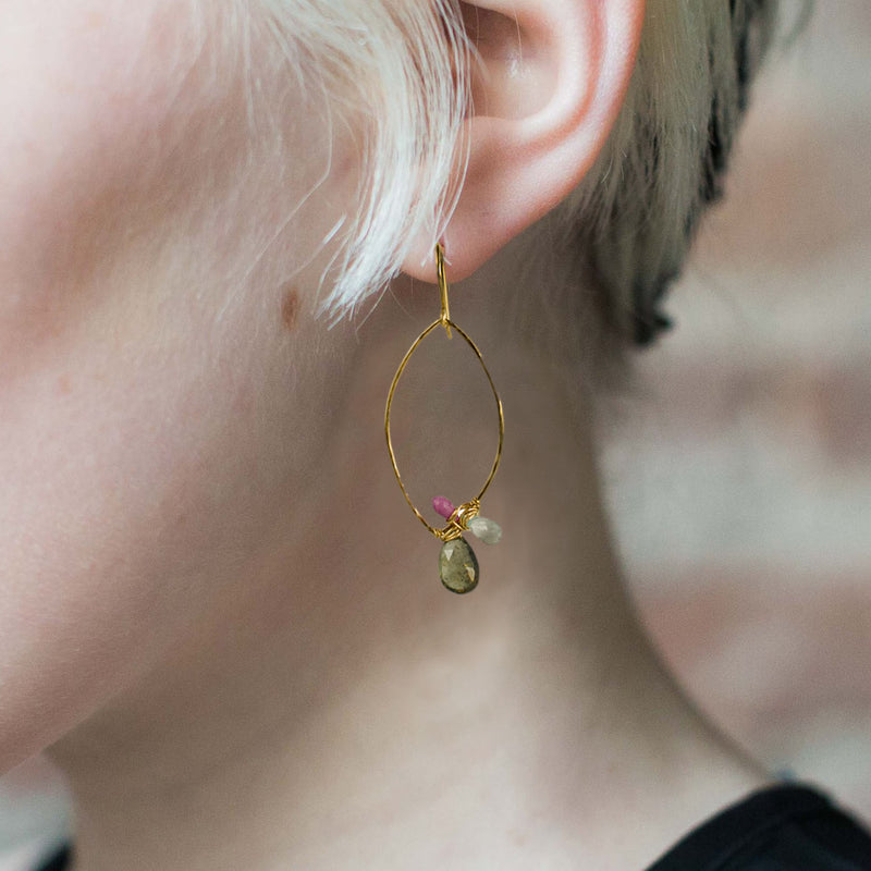 Model wearing gold oval hoop earrings with wrapped gemstones
